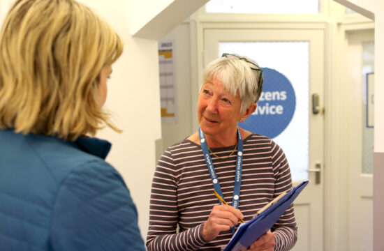 Adult volunteer receptionist with clipboard talking to client.